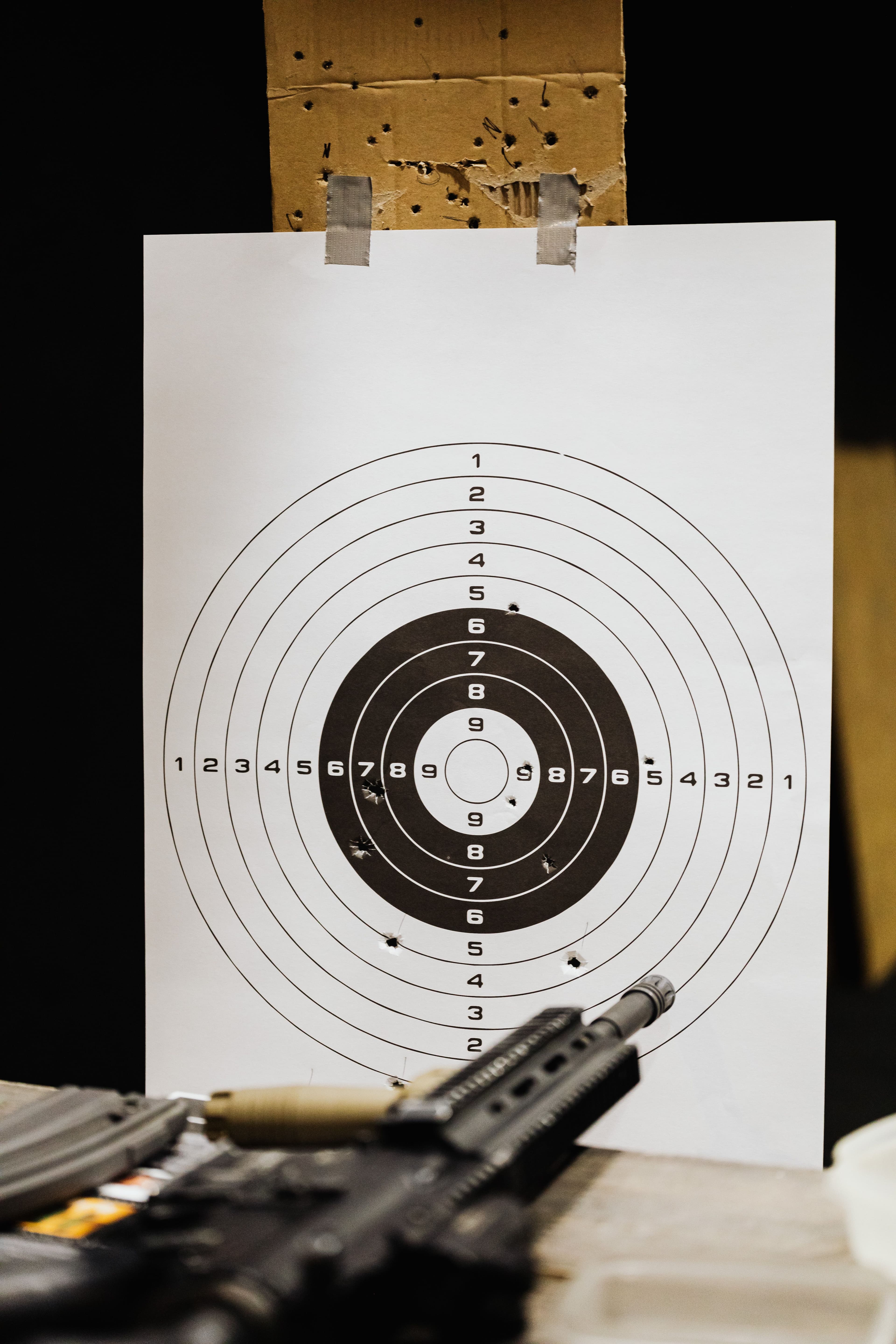 A paper target with a tight bullet grouping and a rifle in the foreground.