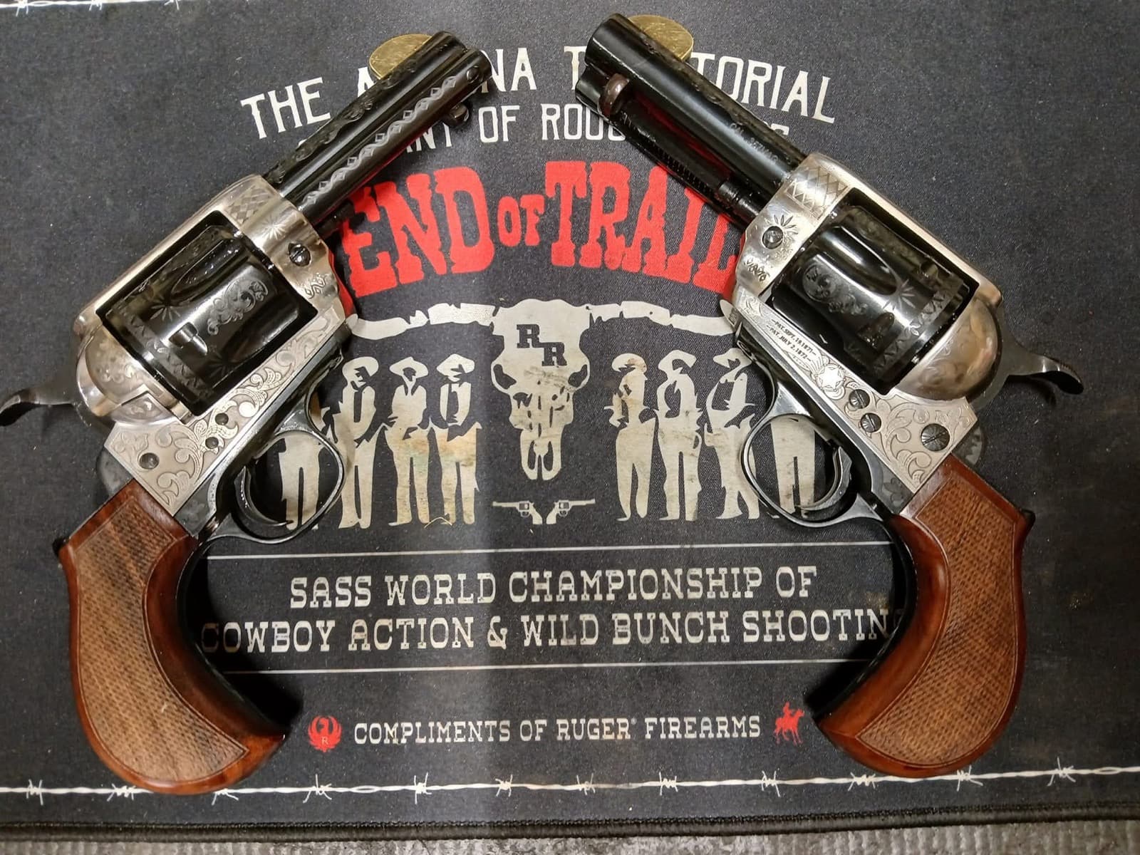 Two engraved single action revolvers resting on a SASS World Championship of Cowboy Action Shooting mat.