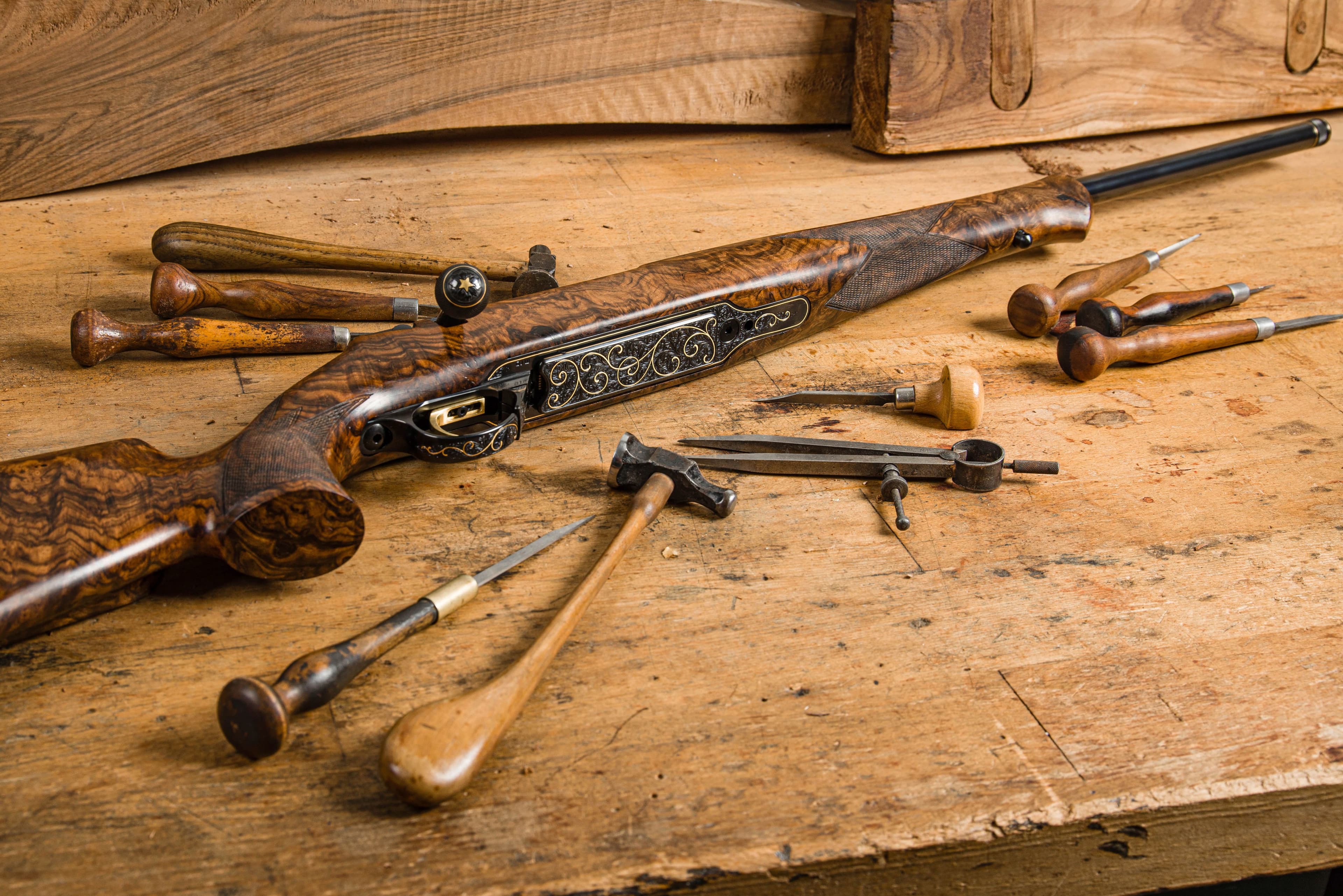 An engraved rifle stock surrounded by traditional gunsmith engraving tools.