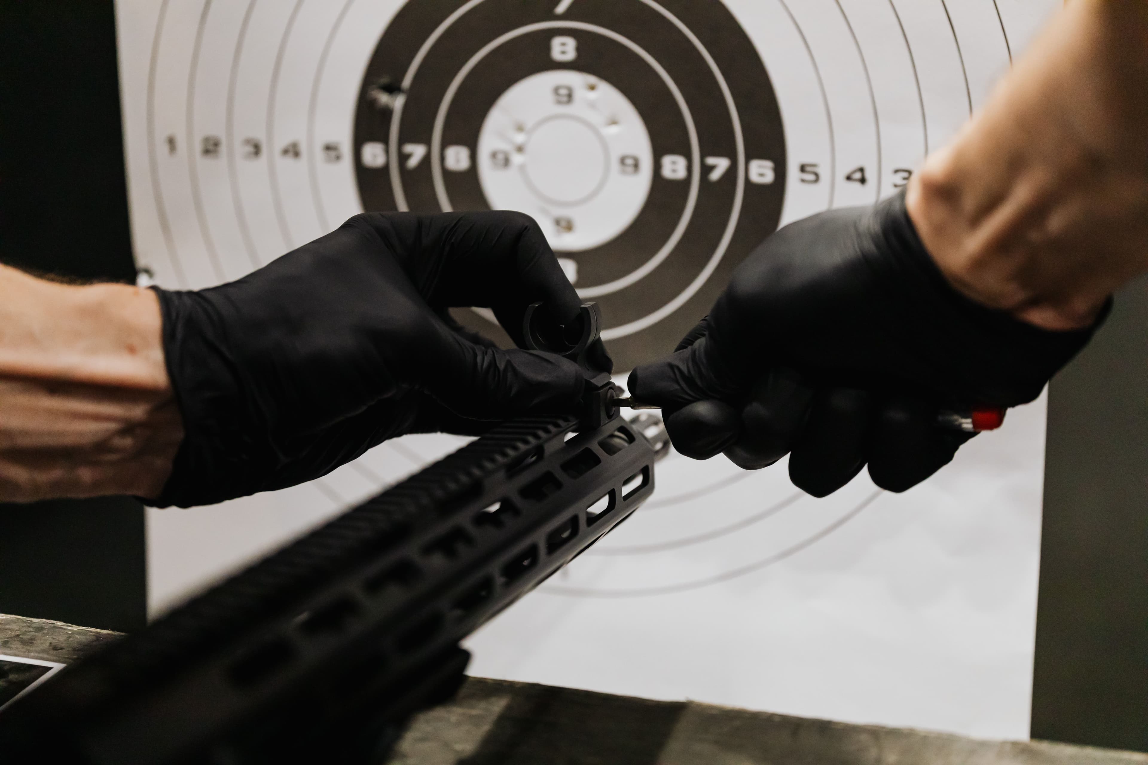 Gloved hands install a front sight component on an AR-style rifle.